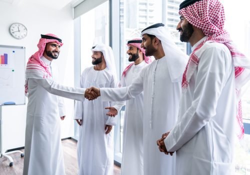 Arab businessmen wearing emirati and saudi kandura meeting in office for business deal - Corporate business group of middle-eastern people working in an international company in middle east
