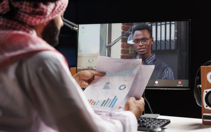 Computer screen takes center stage displaying video call between Muslim businessperson and African-American associate. Picture illustrates the utilization of modern technology by the two individuals.