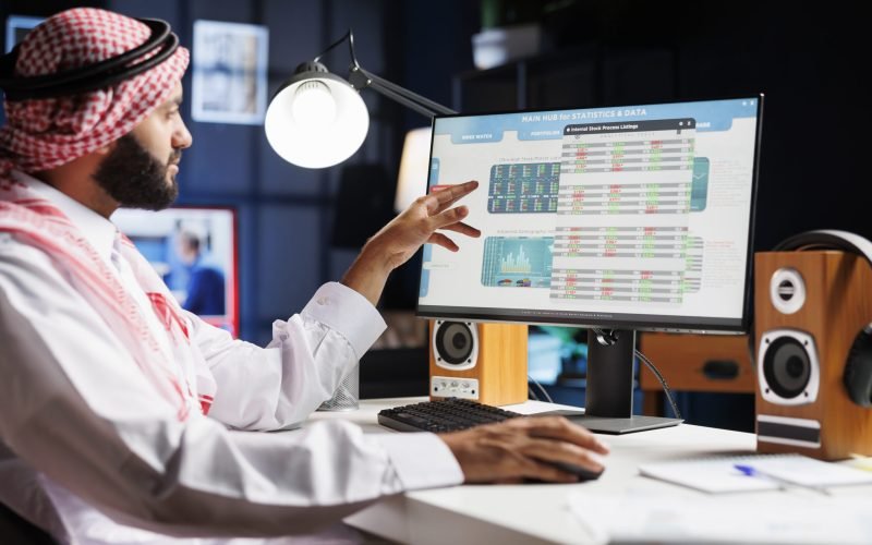 An Arab businessman diligently analyzing data on his computer, making important decisions for the company. Muslim guy wearing traditional attire is checking charts and data on his desktop pc.